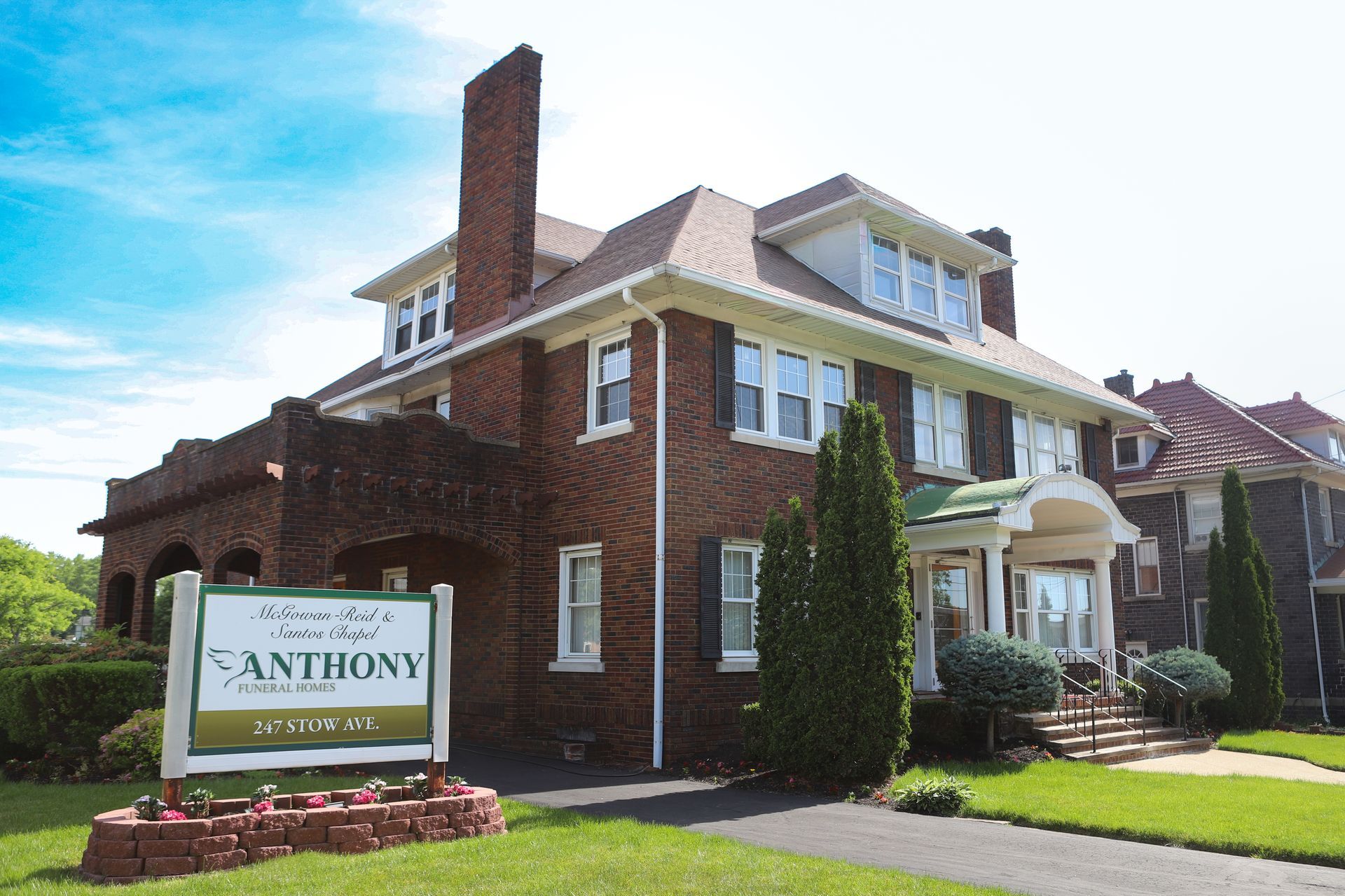 Two-story brick house with white trim, steps, and covered entryway. Green lawn and sidewalk in front.