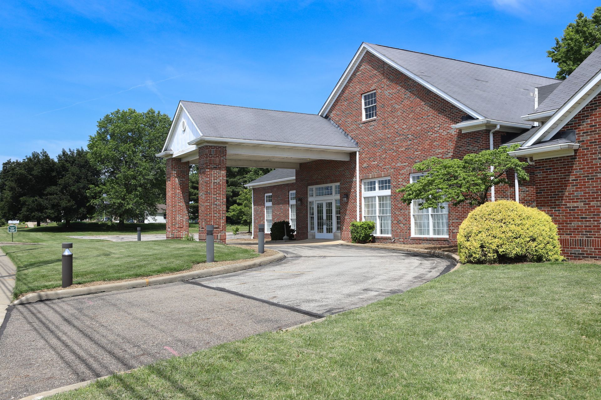 Brick building with covered entrance, small blue car parked out front, green lawn.