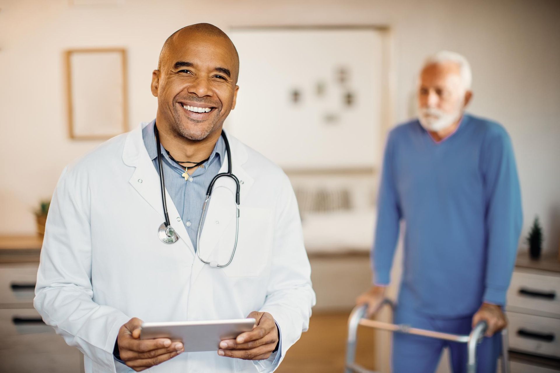 Smiling doctor holding a tablet with an elderly patient using a walker in a clinic room