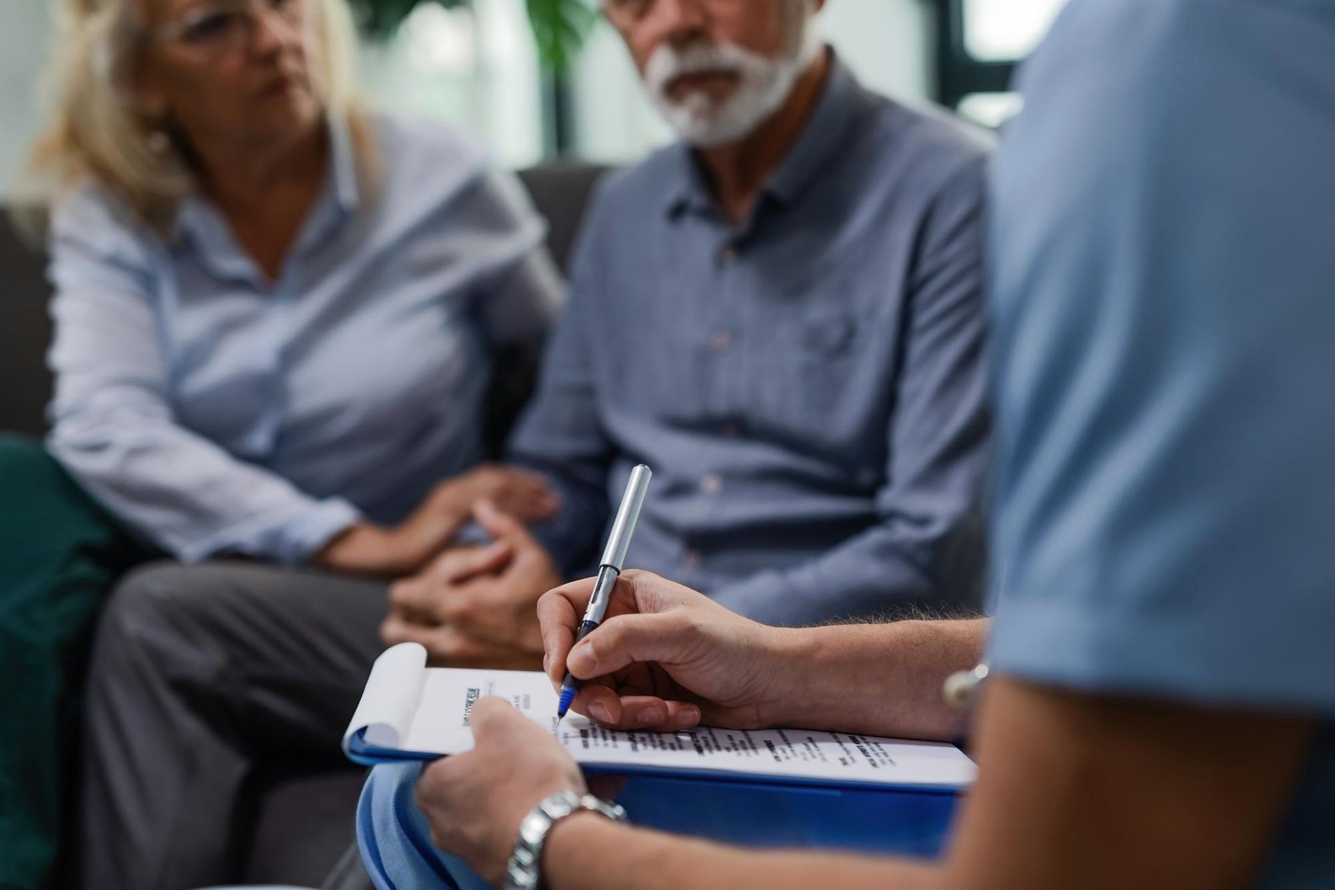 Person taking notes during a small meeting with two seated people in a bright room.