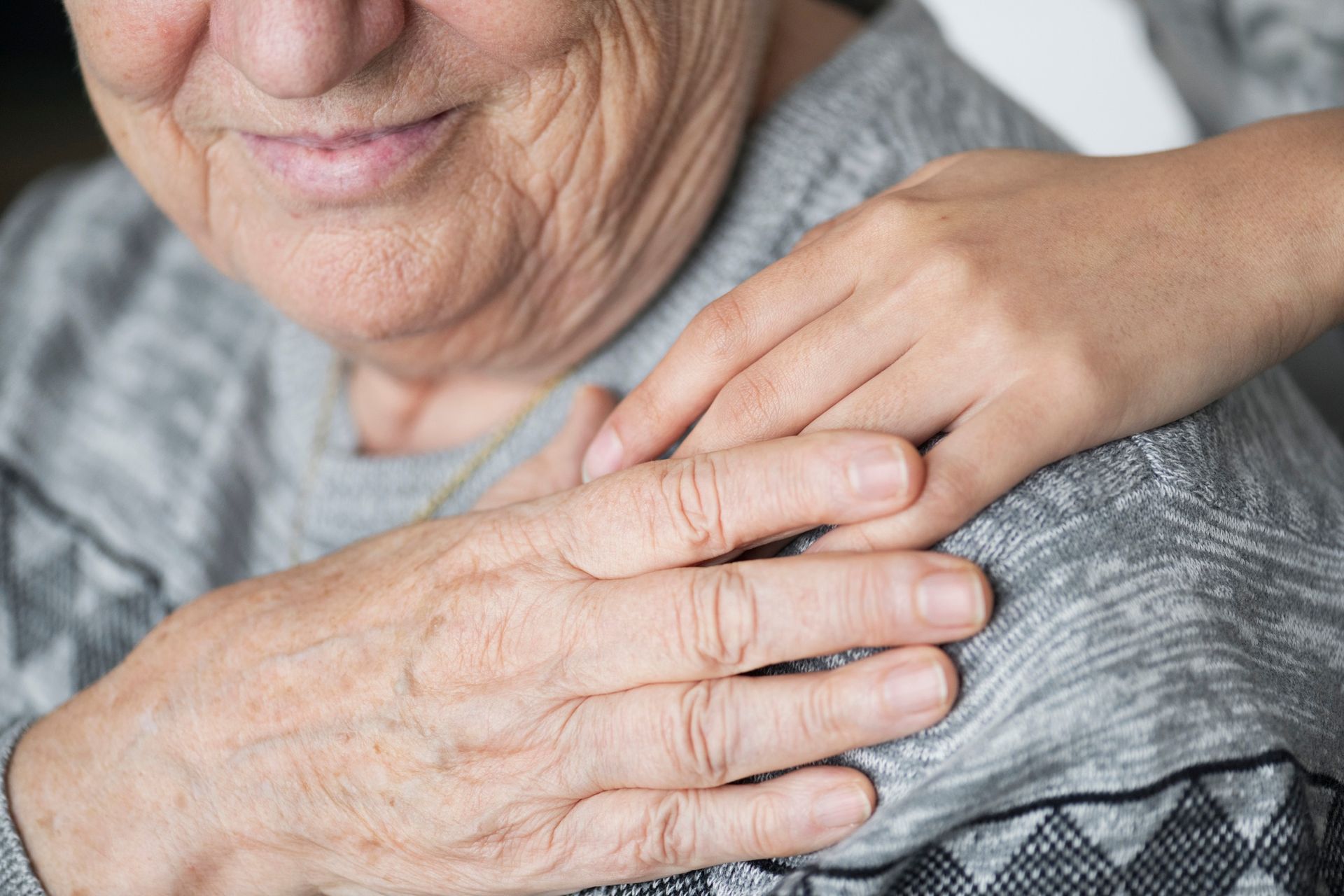 Hand resting gently on an older person’s shoulder in a close-up, comforting gesture