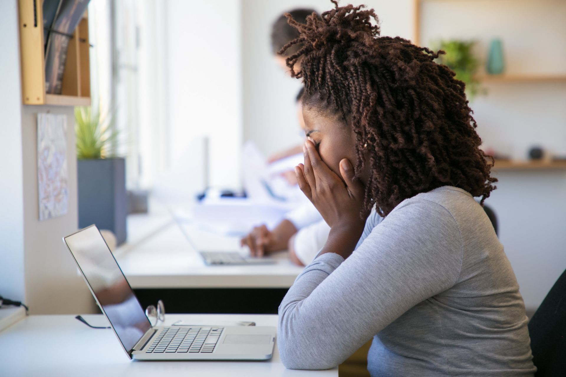 Person seated at a desk, looking worried while using a laptop in a bright office.