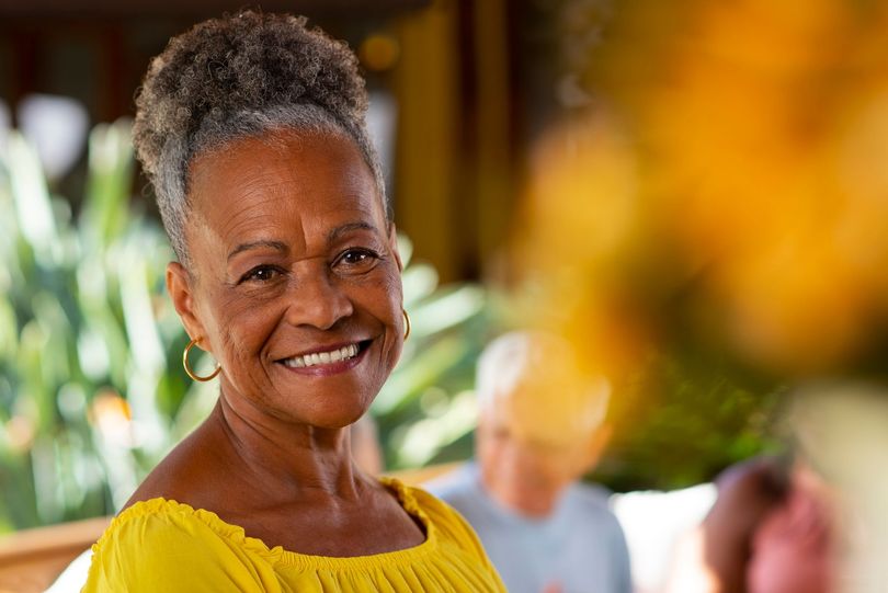 Smiling woman in a yellow top at an outdoor gathering with blurred flowers in the foreground