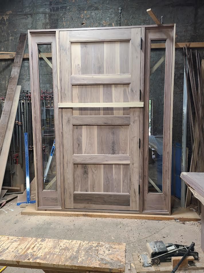 Wooden entryway door with sidelights, natural wood finish, in a workshop setting.
