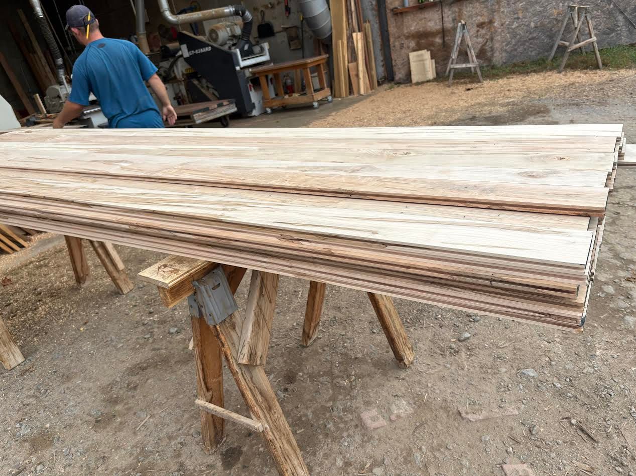 Stack of wooden boards on sawhorse with person in background.