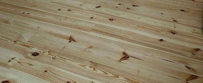 Close-up of wooden floorboards with knots, arranged diagonally. Light brown color.