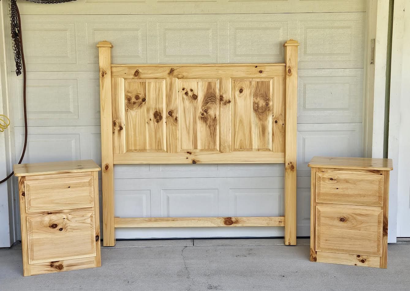 Wooden bed frame with headboard and two nightstands. Set against a white garage door.
