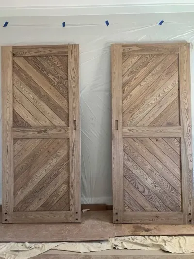 Two light-colored wooden doors with chevron pattern are propped against a wall during installation.