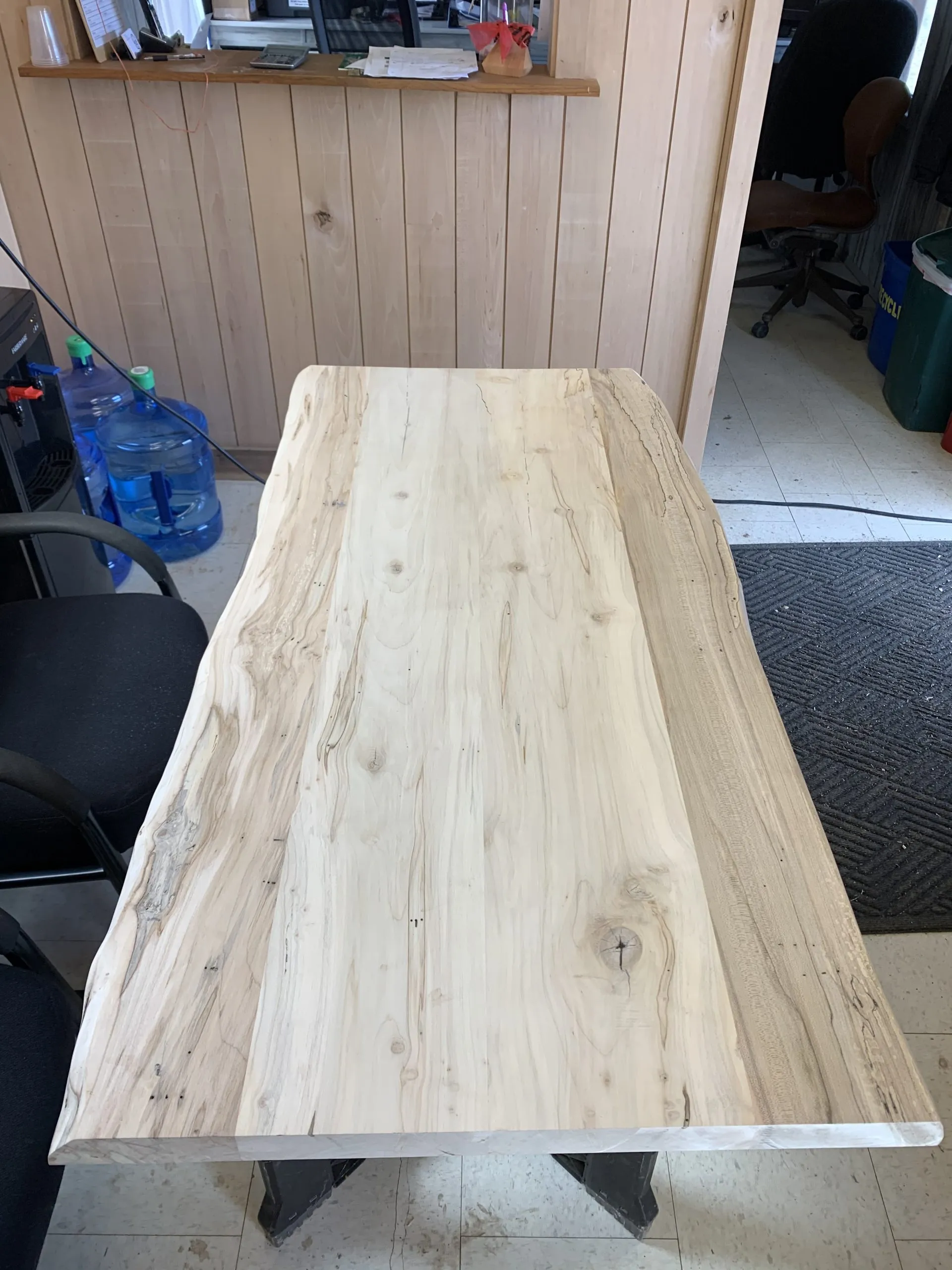 Wooden table with natural edge, light wood, in a workshop setting.