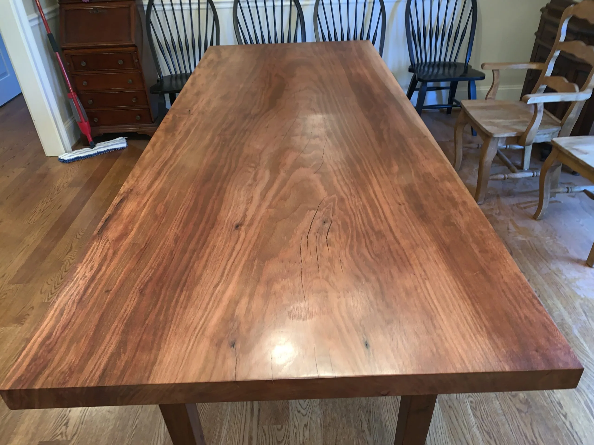 Large, rectangular wooden dining table with a glossy finish. Chairs are in the background.