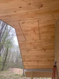 Wooden ceiling of a porch with two wires running along the boards; outdoor setting.