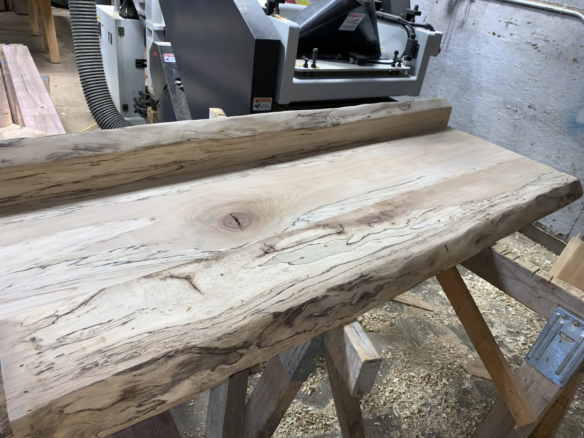 Wooden slab being planed with a large machine in a workshop setting.