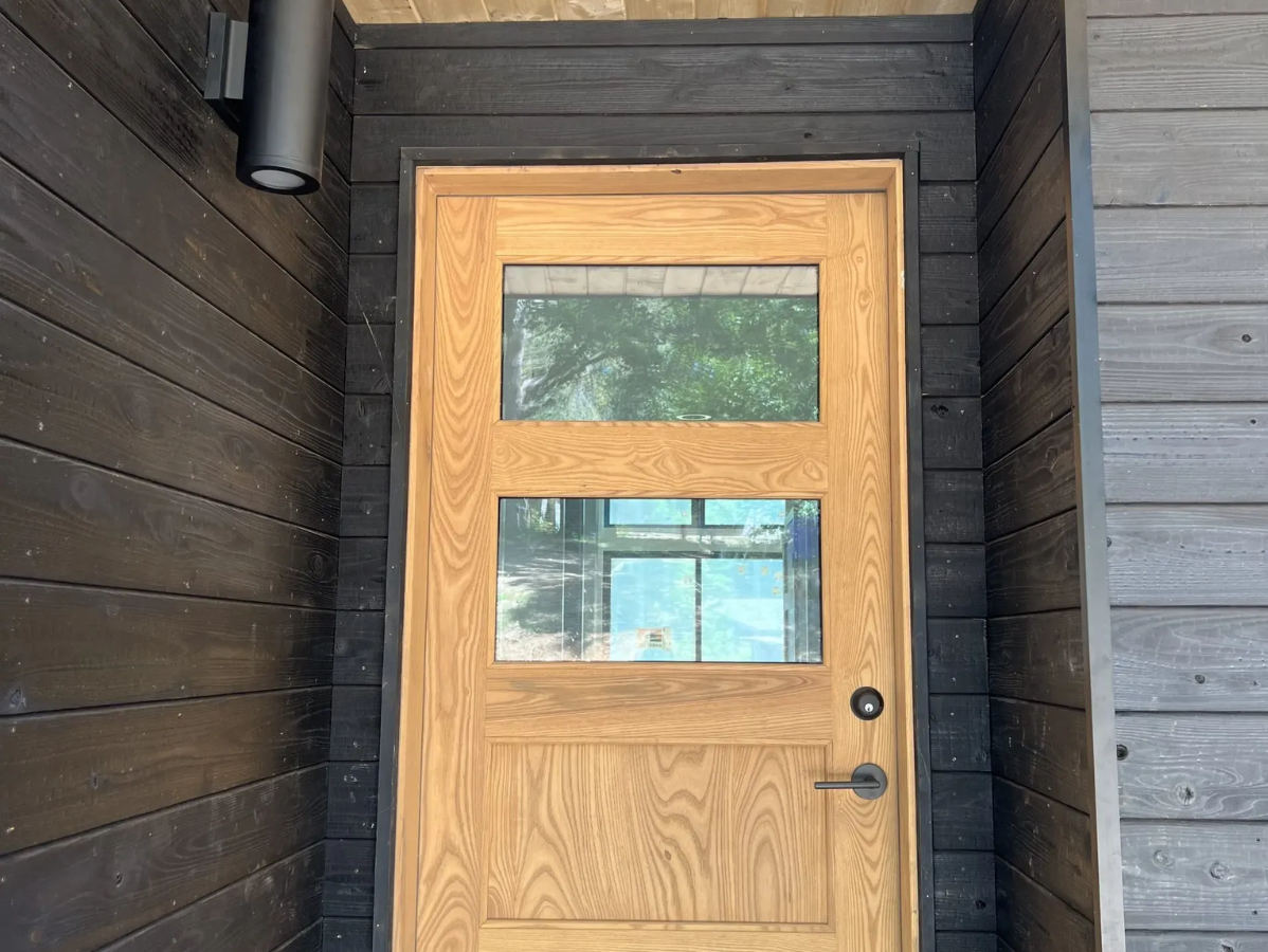 Wooden door with two glass panels and a silver handle, surrounded by dark wood siding.