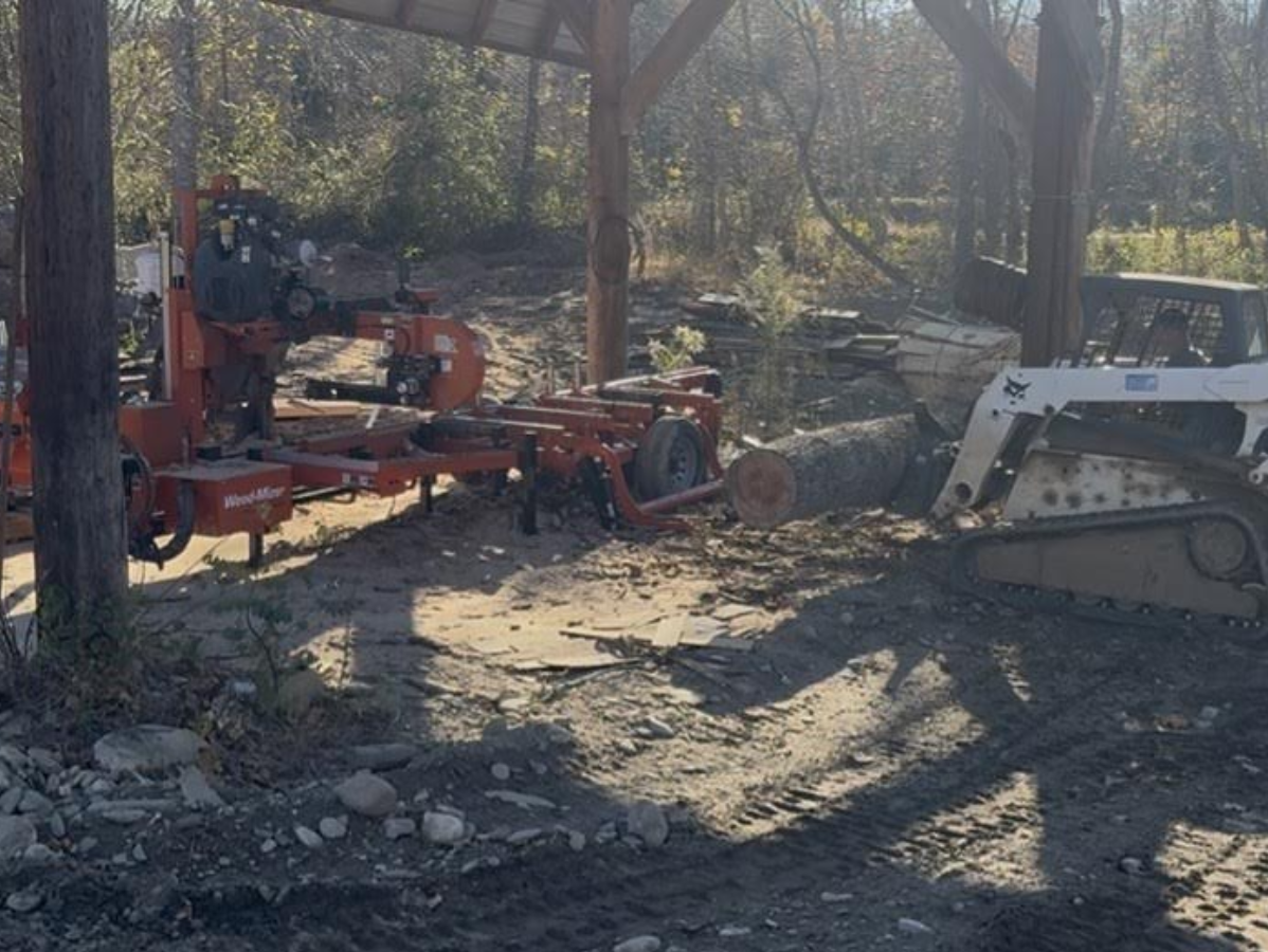 Sawmill with a log and a skid steer under a wooden shelter.