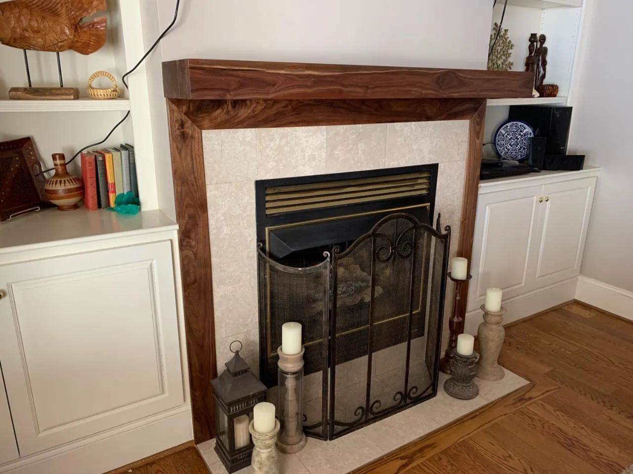 Fireplace with dark wooden mantel, surrounded by light stone and built-in white cabinets.