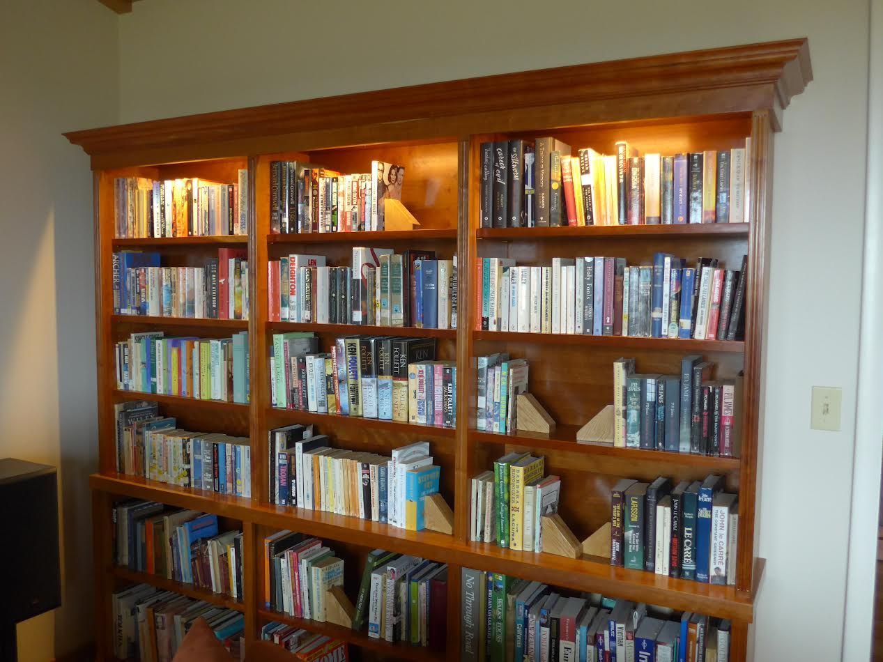 Wooden bookcase filled with books, lit from above, against a white wall.
