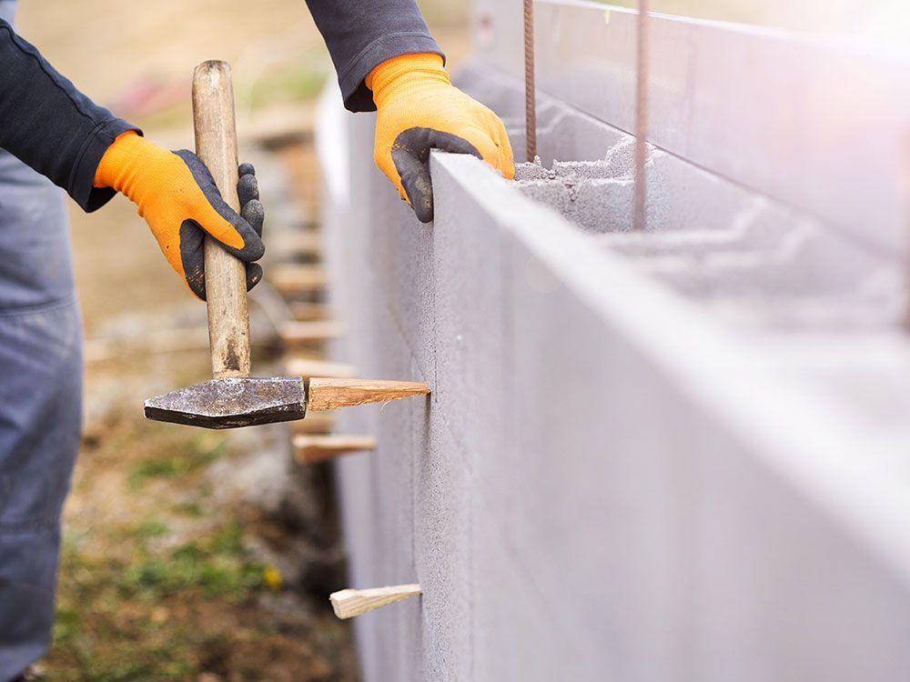 a person wearing orange gloves is holding a hammer working on a concrete
