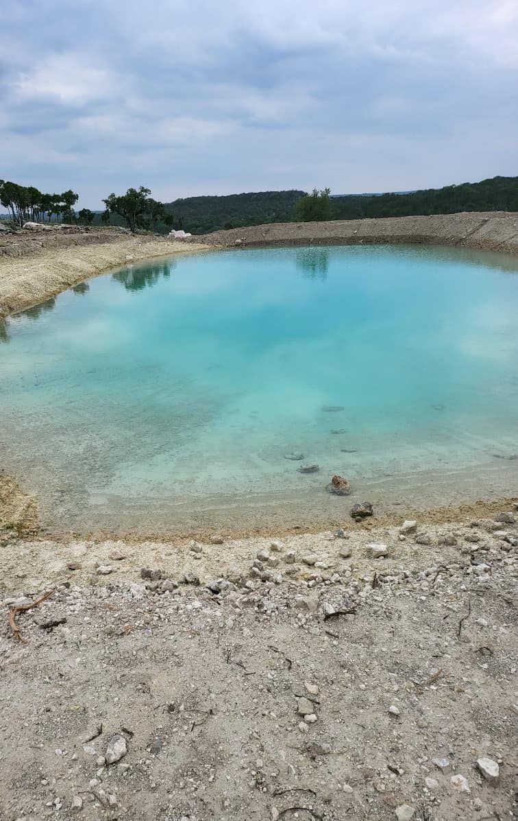 Turquoise water-filled quarry pond with rocky shores under a cloudy sky