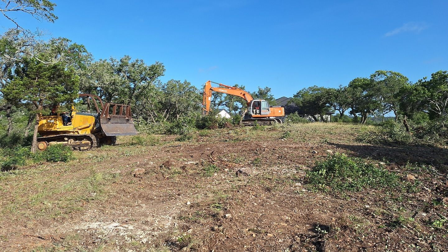 Excavators clearing brush on a dirt lot under a clear blue sky