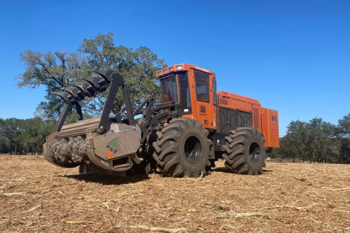 Orange forestry machine mulching brush in a dry field under a blue sky