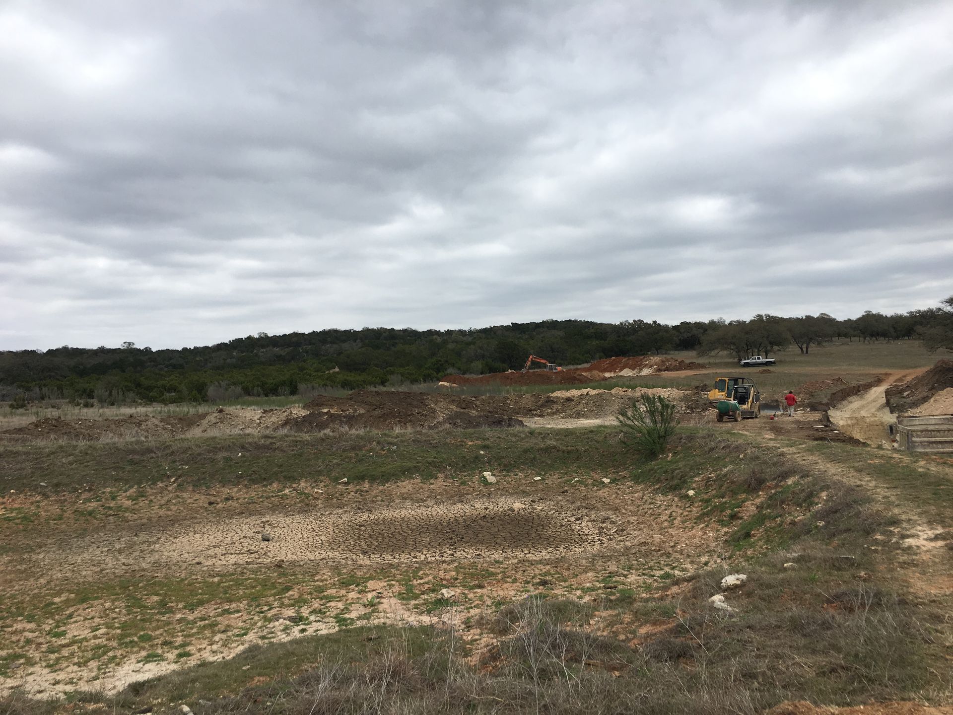 Open quarry landscape under cloudy sky, with dirt roads and small machinery in the distance