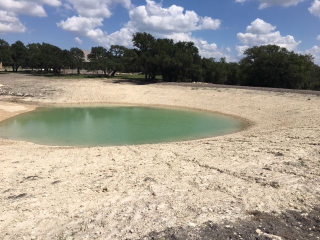 Small turquoise pond in a dry sandy landscape with trees in the background