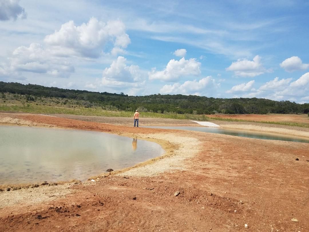 Mud lake shoreline under a partly cloudy sky, with one person standing in the distance.