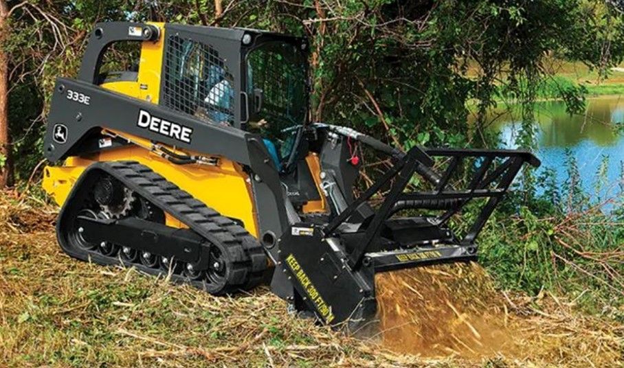Yellow John Deere tracked skid steer clearing brush near water