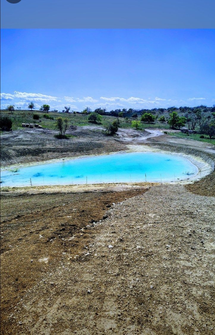 Turquoise pond beside a dirt path in a dry, open landscape under a blue sky