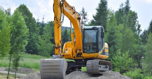 Yellow excavator on a dirt mound in a wooded area