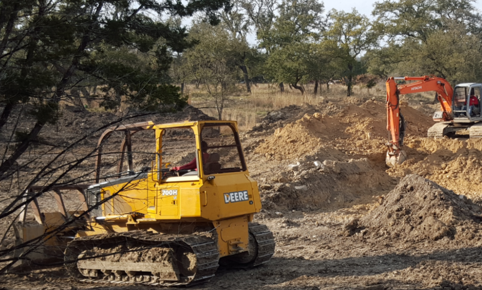 Two excavators working on a dirt hillside, one yellow in the foreground and one orange in the background.