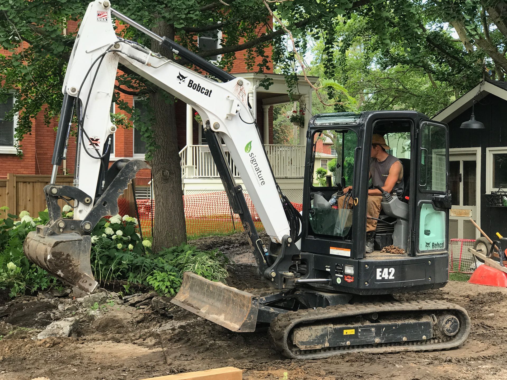 A man is driving a small excavator in front of a house.