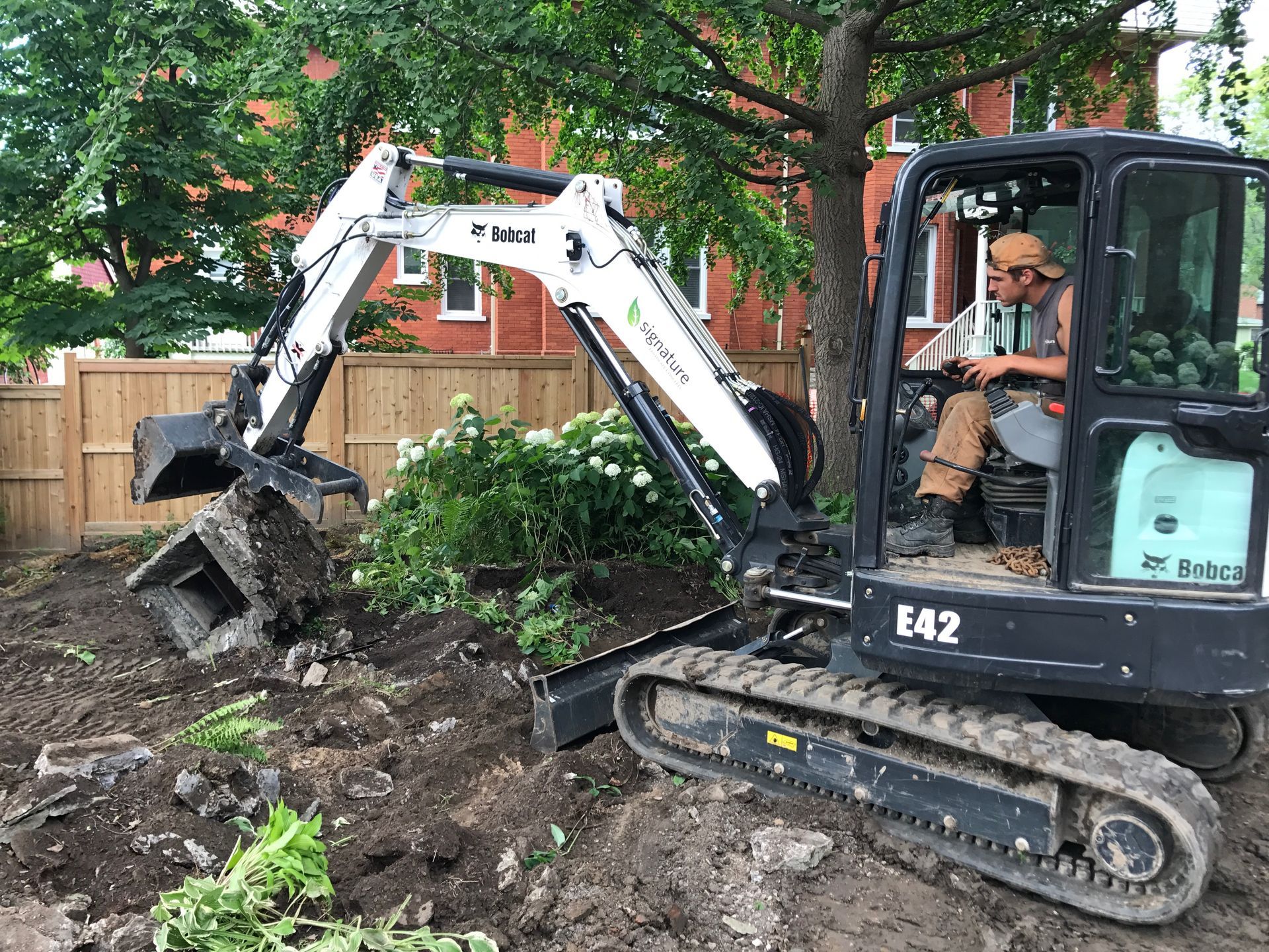 A man is driving a small excavator in a yard.