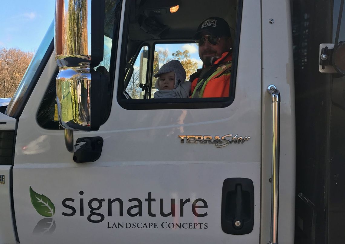A man and a child are sitting in the driver 's seat of a signature truck.
