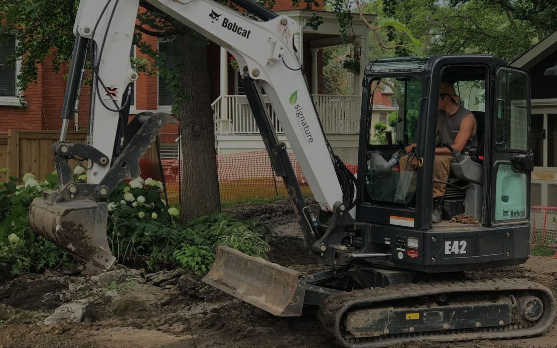 A man is driving a bobcat excavator on a dirt road.