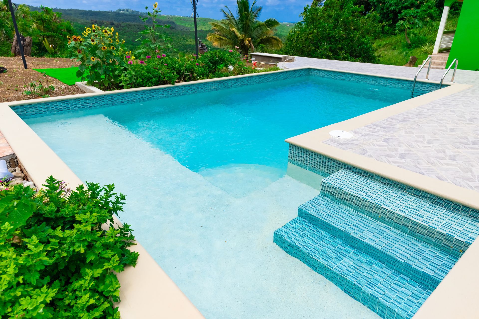 Outdoor turquoise swimming pool with steps and lush green landscaping surrounding it