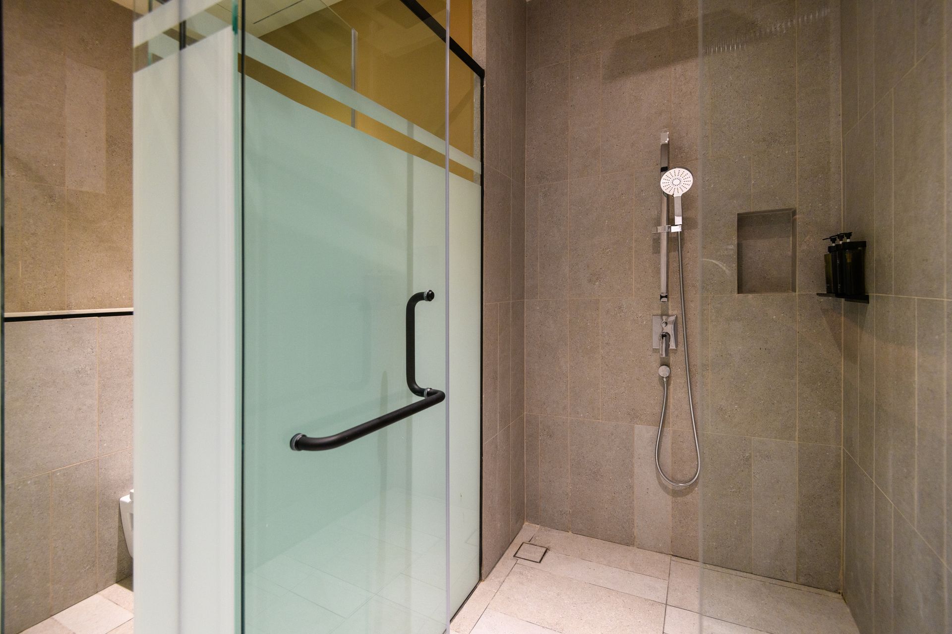 Modern shower area with glass enclosure and wall-mounted showerhead in a tiled bathroom.