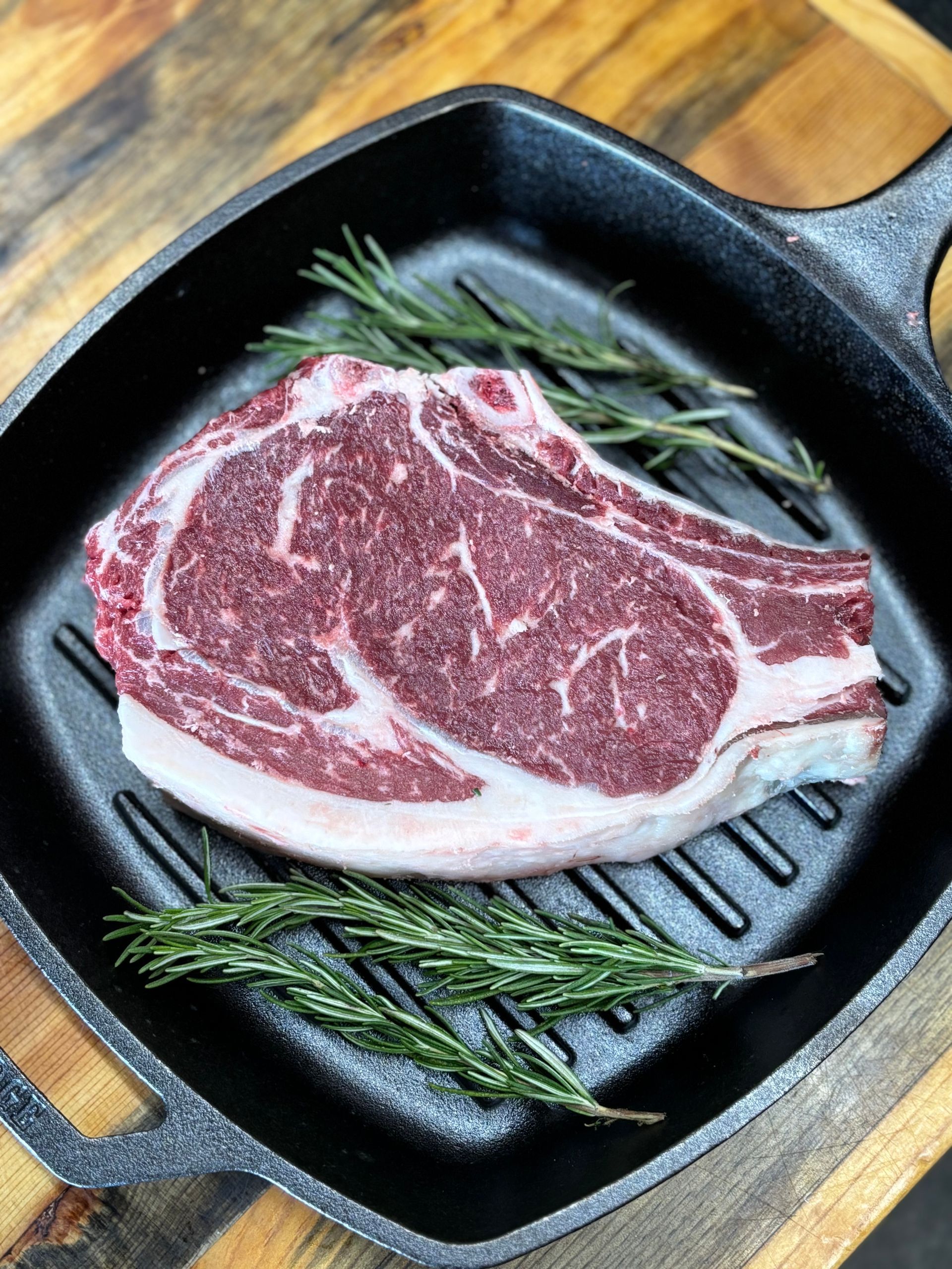 A steak is sitting on top of a cast iron skillet on a wooden table.