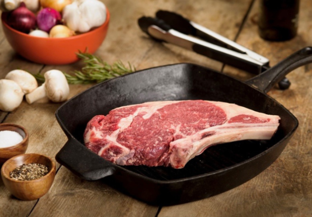 A piece of raw meat is in a skillet on a wooden table