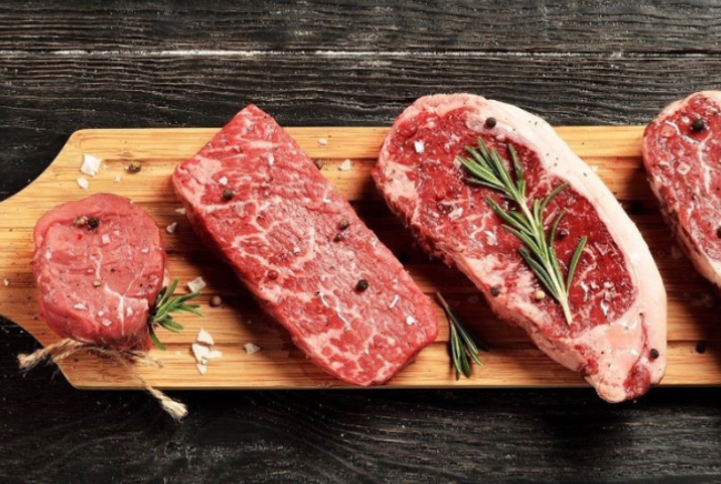 A wooden cutting board topped with a variety of raw steaks.