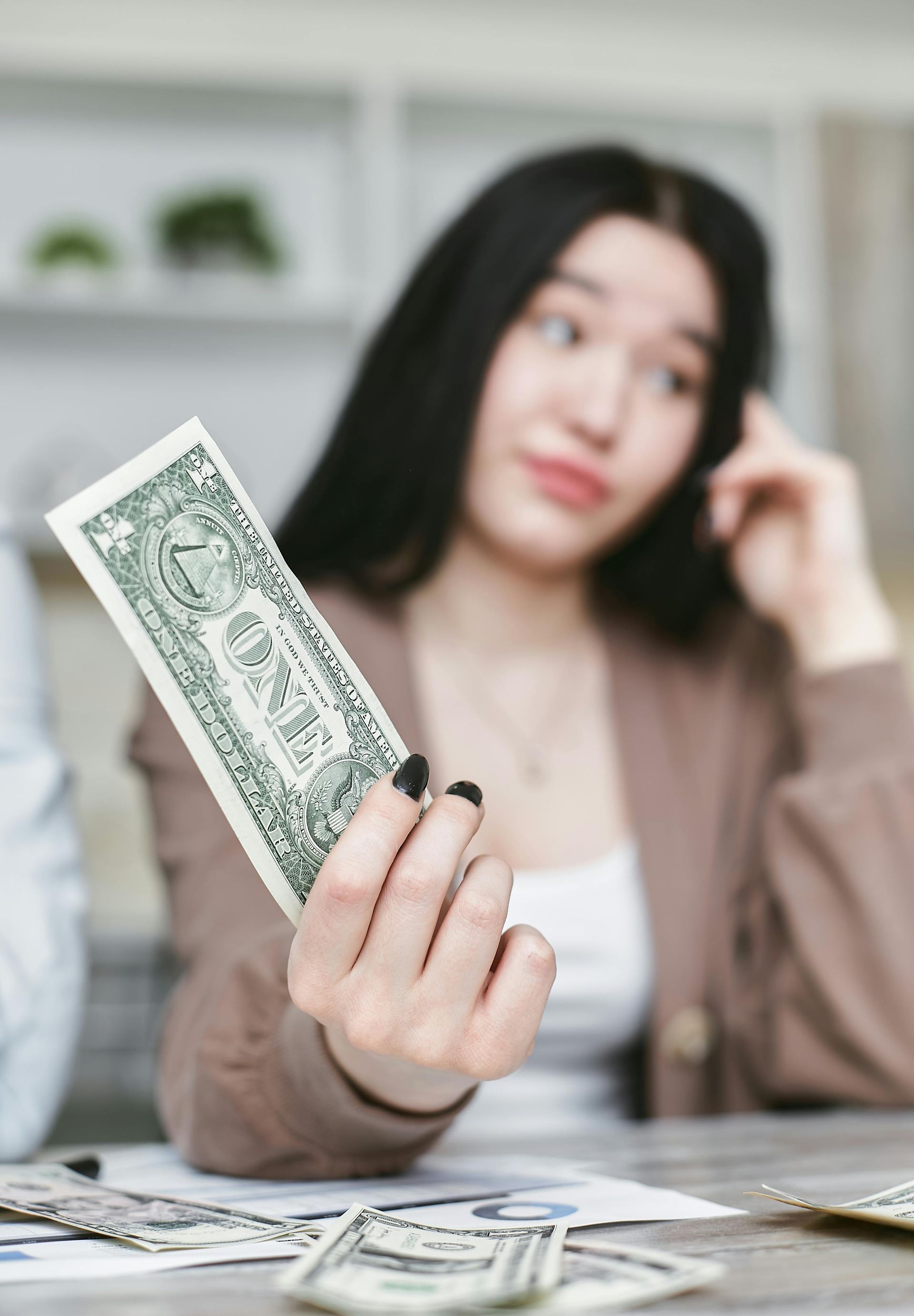 Person holding a dollar bill at a table with more cash, indoors, looking to the side