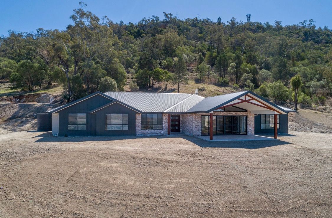 Modern single-story house with a grey roof, brick facade, and large patio, set in a dry, hilly landscape with trees — L & K Electrical & Air Conditioning in Narrabri, NSW