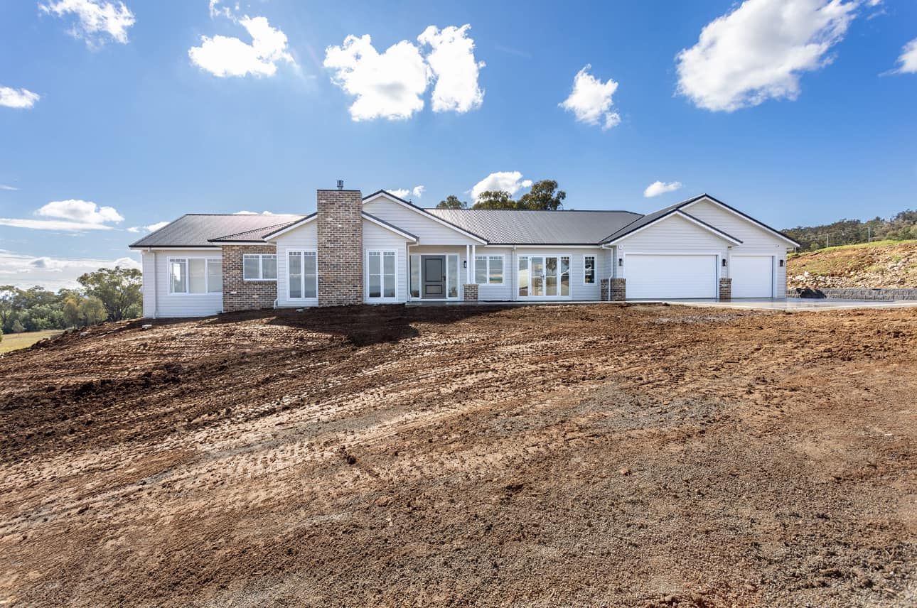 A light blue house with a white garage on a hill under a blue sky with clouds — L & K Electrical & Air Conditioning in Gunnedah, NSW