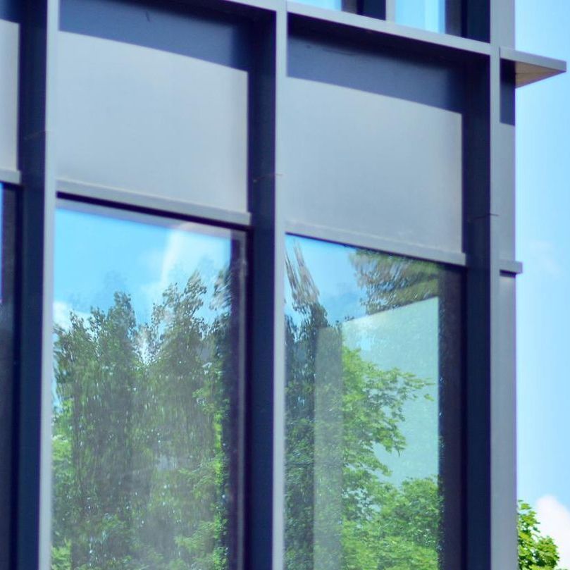 A building with a lot of windows and trees reflected in the windows