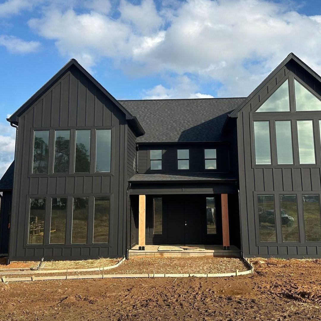 A large black house with a lot of windows is sitting on top of a dirt field.
