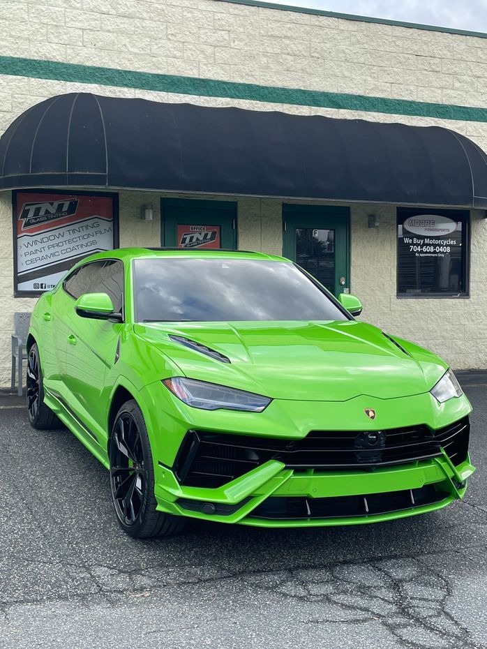 A green lamborghini urus is parked in front of a building.