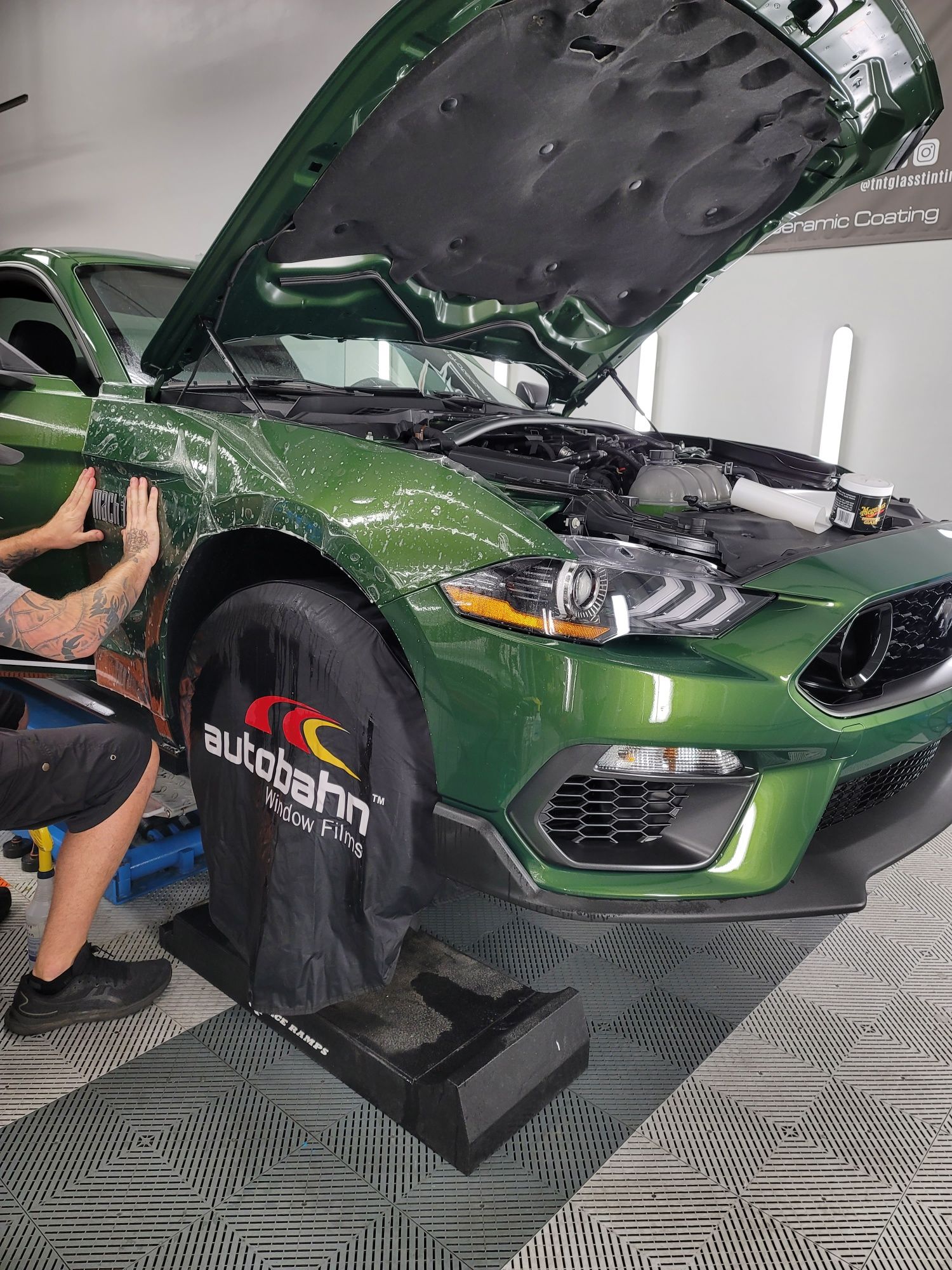 A person is applying a protective film to the hood of a blue car.