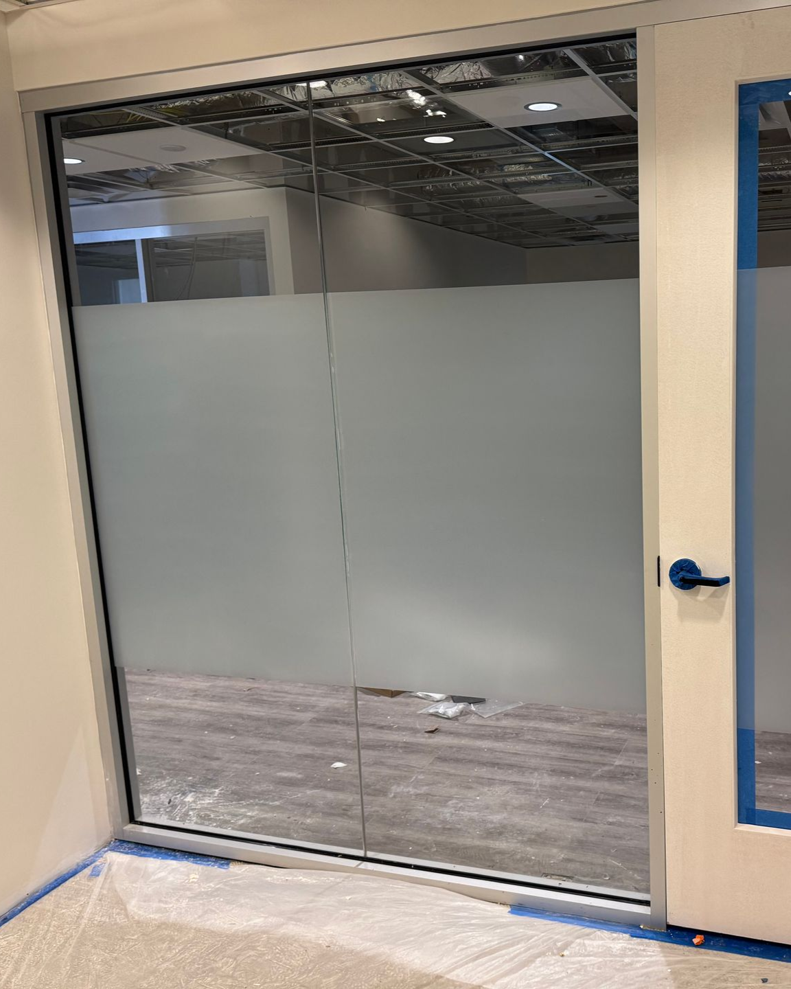 Two glass office panels with frosted privacy film installed in a light-colored frame next to a closed door.