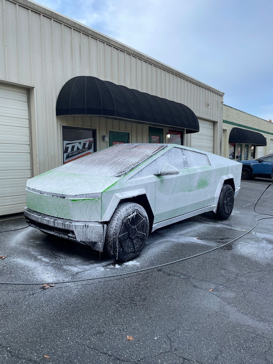 A tesla cybertruck is covered in foam in front of a building.