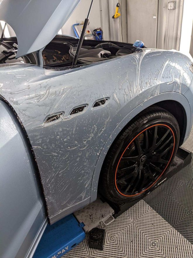 A car with the hood open is sitting on a lift in a garage.